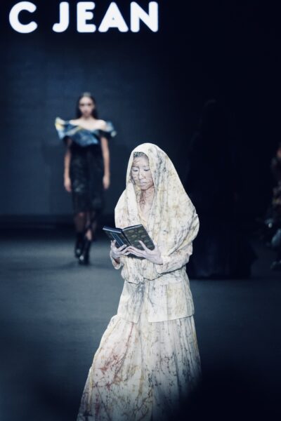 C JEAN 26AW 臺北時裝週開幕秀中，焦點模特兒手持《普門品》經書緩步登場，透過臈纈染服裝與靜謐儀式感，詮釋生命循環與內在覺知的哲學意境。圖/主辦單位