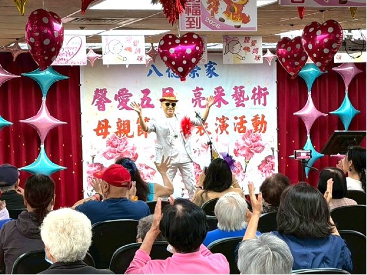 《圖說》亮采藝術關懷團隊表演者於舞台上帶動氣氛（前方），透過熱情演出與互動引領住民長輩一同揮手響應，現場掌聲與笑聲不斷，洋溢歡樂與感動。〈八德榮家提供〉