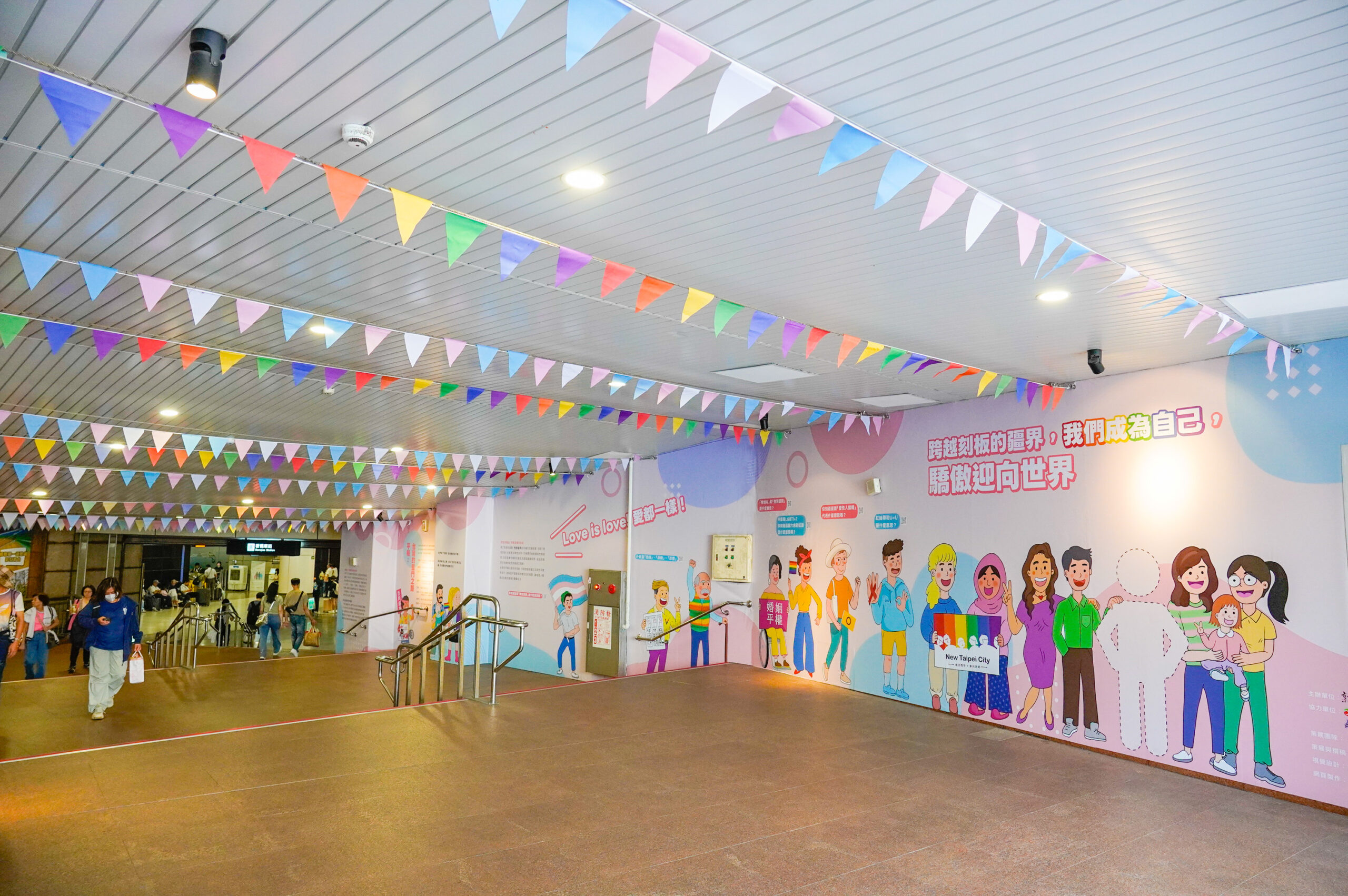 《圖說》今日至6月21日期間，「愛在新北・驕傲同行」特展於新北市民廣場往板橋車站的連通道展開，並懸掛多元性別友善旗幟，象徵城市裡的友善包容。〈社會局提供〉
